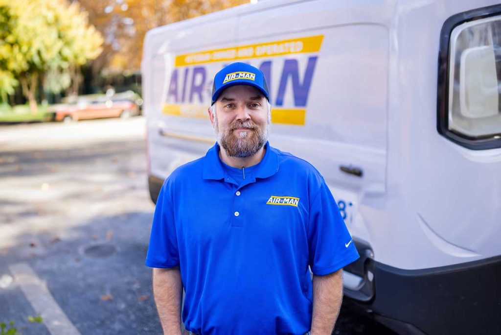 Air-Man Heating and Air technician standing beside a company van