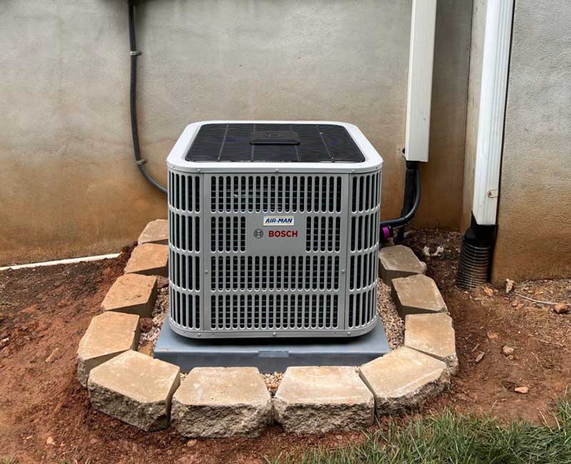 Outdoor air conditioner unit set on a stone paver pad next to a house