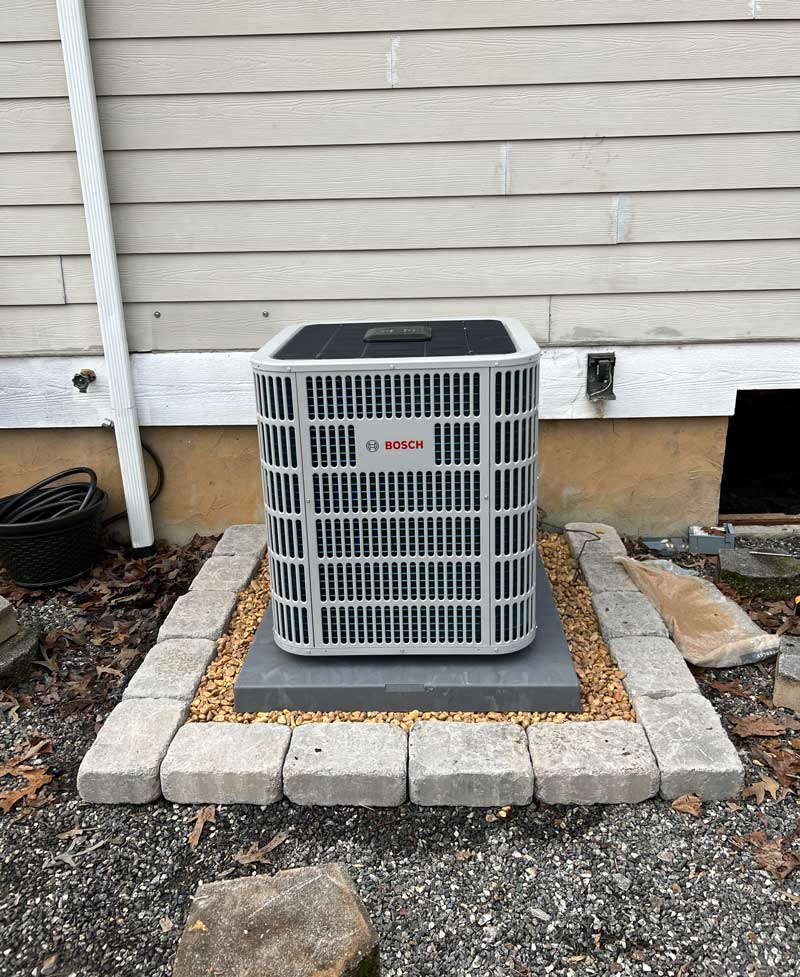 Newly installed outdoor air conditioning unit on a gravel bed beside a home