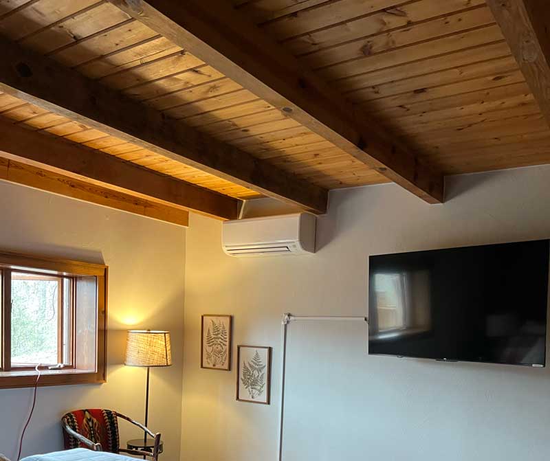 Ductless mini split head mounted on the wall of a room with a wood-beam ceiling